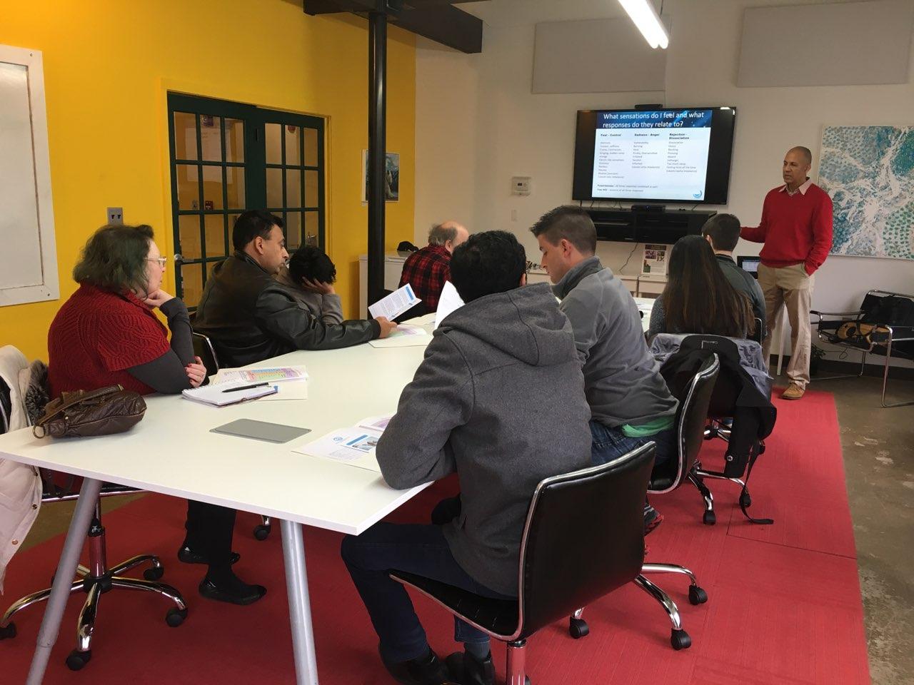 Um facilitador guiando um grupo sentado por um slide sobre sensações e respostas durante uma sessão de formação HEAL